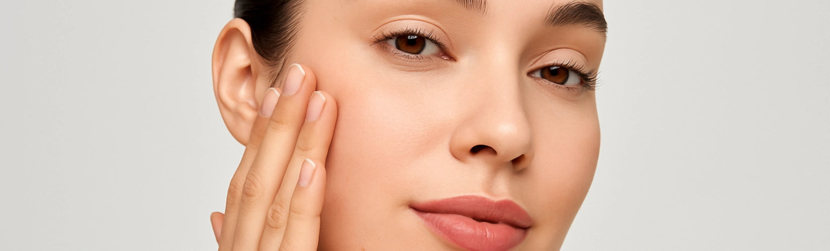 Junge Frau mit gesunder, gepflegter Haut vor neutralem Hintergrund – Symbolbild für moderne Gesichtspflege